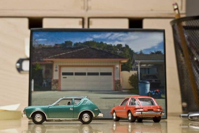 Editorial product photography of toy cars with a suburban landscape background.